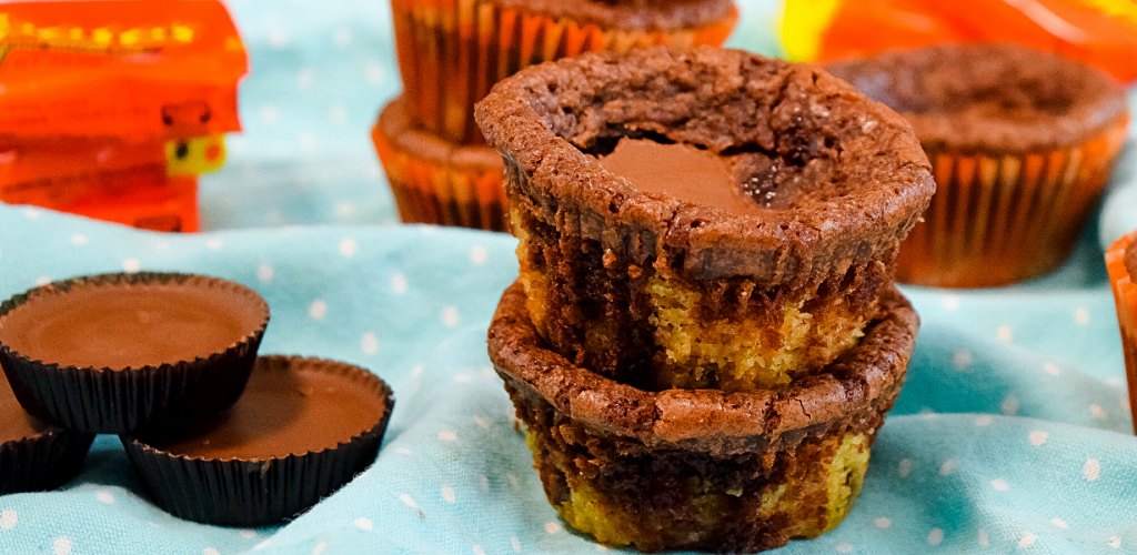Two peanut butter stuffed brownie cookie cups stacked on top of each other next to peanut butter cups on a blue polka dot towel