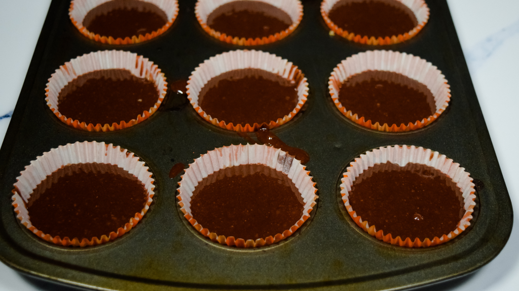 A muffin tin with orange cupcake liners full of brownie batter. 