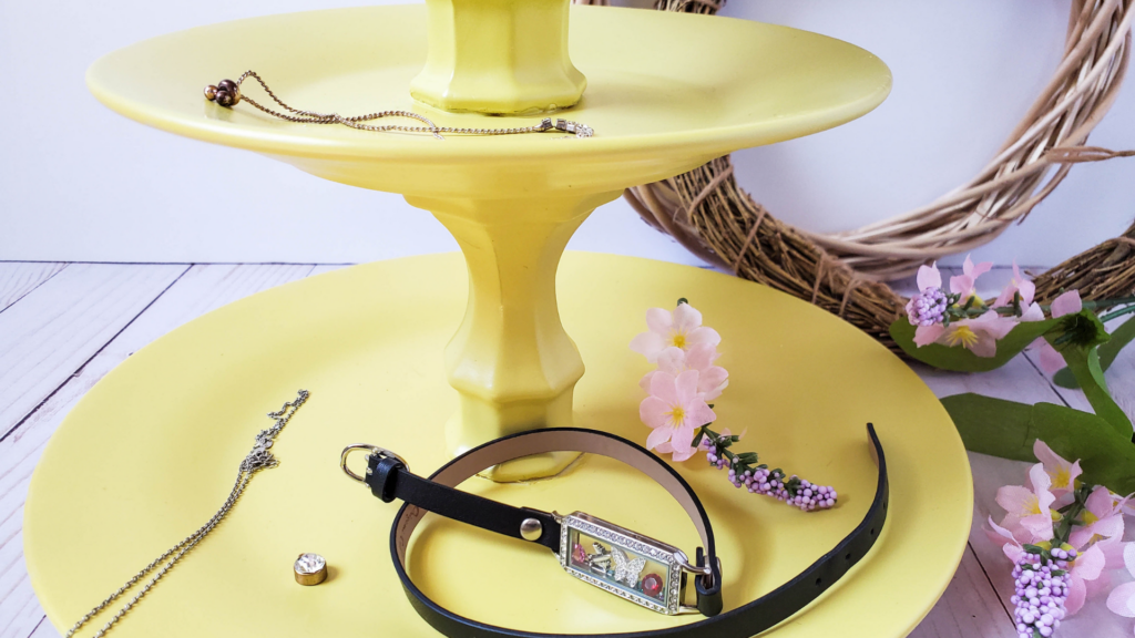 A close up of the bottom two layers of the yellow finished dollar store tiered tray with a watch and flowers and jewelry.